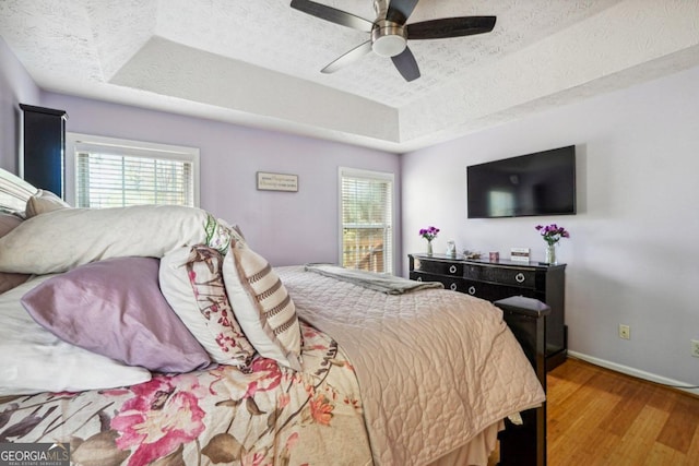 bedroom with hardwood / wood-style flooring, ceiling fan, a textured ceiling, and a raised ceiling