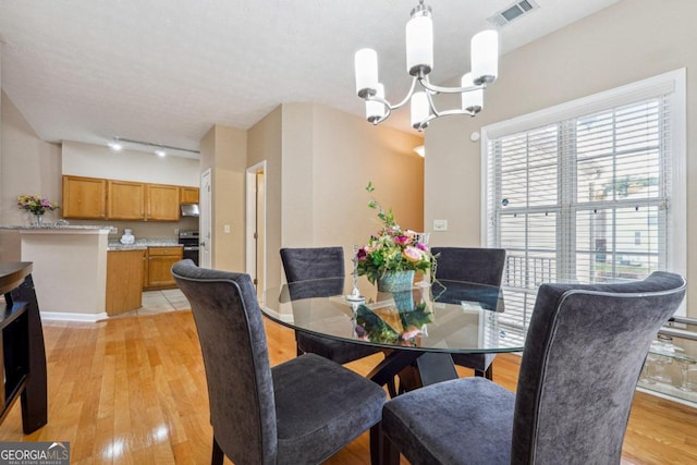 dining area with a chandelier, a textured ceiling, track lighting, and light hardwood / wood-style flooring