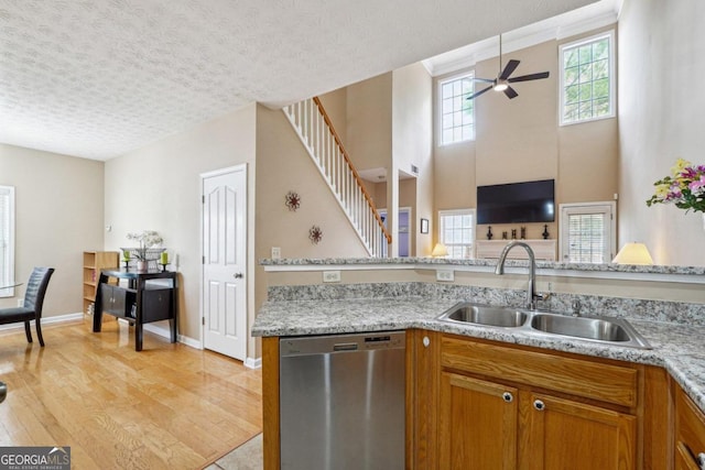 kitchen with a textured ceiling, light hardwood / wood-style floors, stainless steel dishwasher, and sink