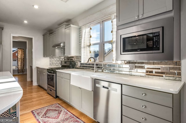 kitchen with tasteful backsplash, gray cabinets, sink, light hardwood / wood-style flooring, and appliances with stainless steel finishes