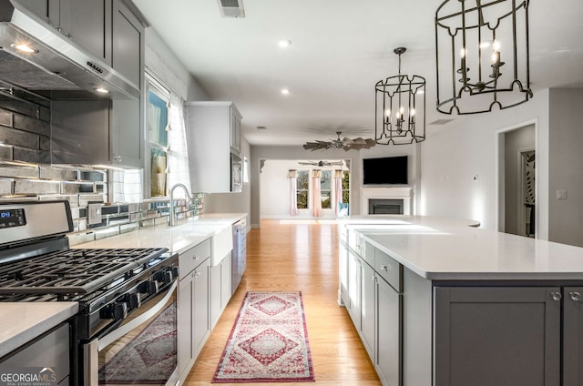 kitchen with a center island, stainless steel gas stove, hanging light fixtures, gray cabinets, and light hardwood / wood-style flooring