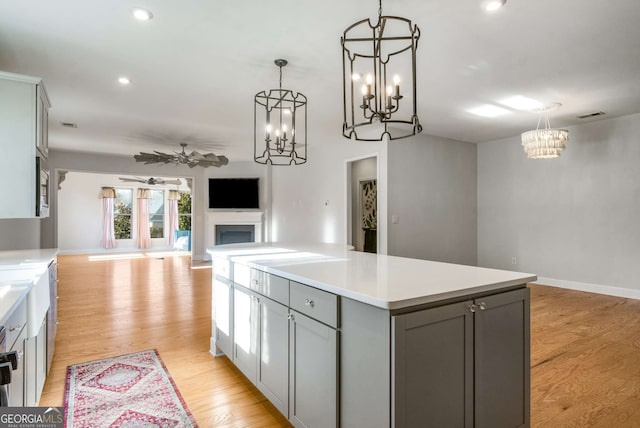 kitchen featuring gray cabinets, pendant lighting, a center island, light wood-type flooring, and ceiling fan with notable chandelier