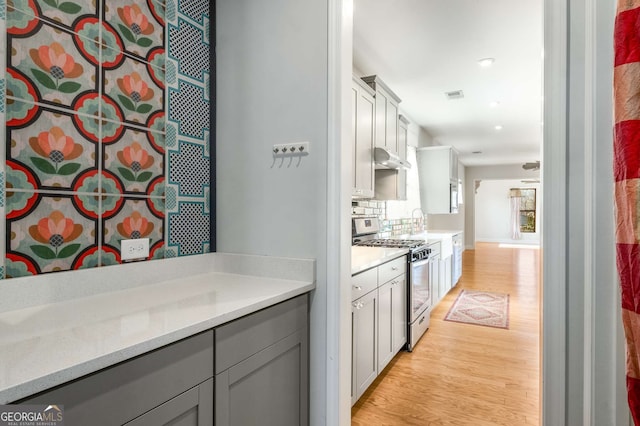 kitchen with gray cabinetry, tasteful backsplash, light wood-type flooring, stainless steel gas stove, and light stone counters