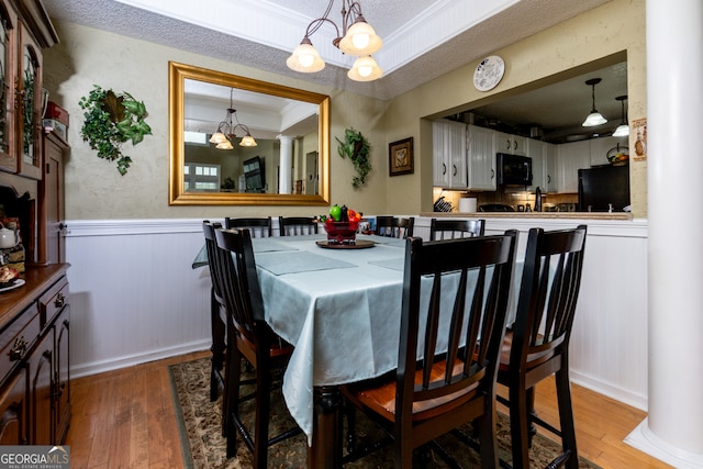 dining area featuring ornate columns, an inviting chandelier, hardwood / wood-style floors, a textured ceiling, and crown molding