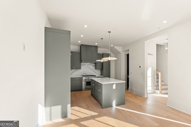 kitchen featuring gray cabinetry, a center island, light hardwood / wood-style flooring, pendant lighting, and decorative backsplash