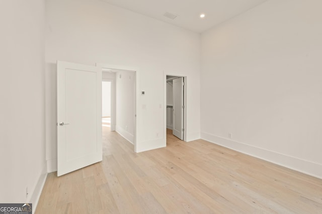 unfurnished bedroom with a walk in closet, baseboards, light wood-type flooring, and a towering ceiling