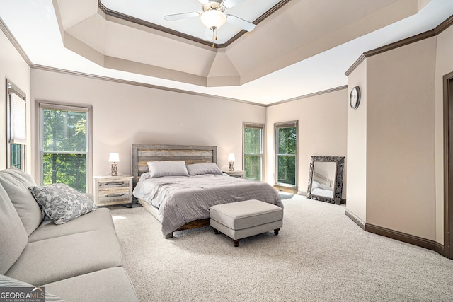 carpeted bedroom with a tray ceiling, multiple windows, ceiling fan, and crown molding