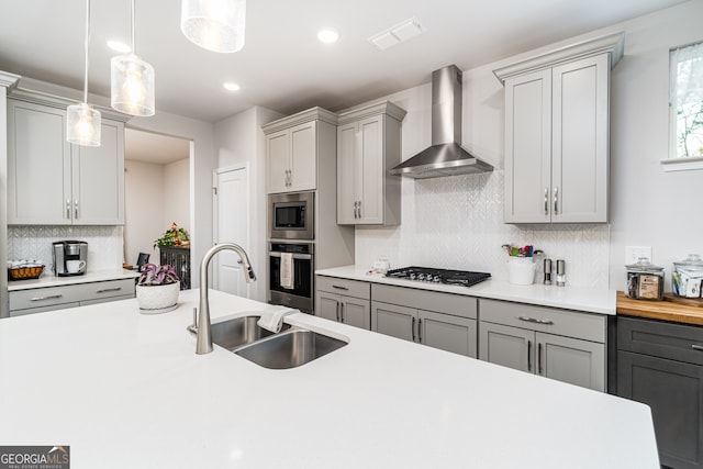 kitchen featuring gray cabinetry, wall chimney exhaust hood, stainless steel appliances, sink, and hanging light fixtures