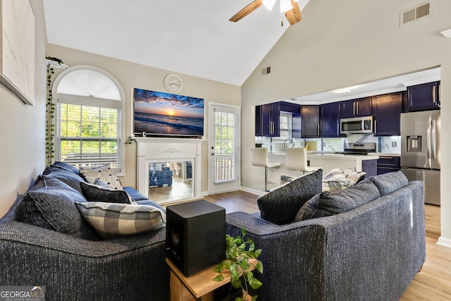 living room featuring light hardwood / wood-style flooring, high vaulted ceiling, ceiling fan, and a healthy amount of sunlight