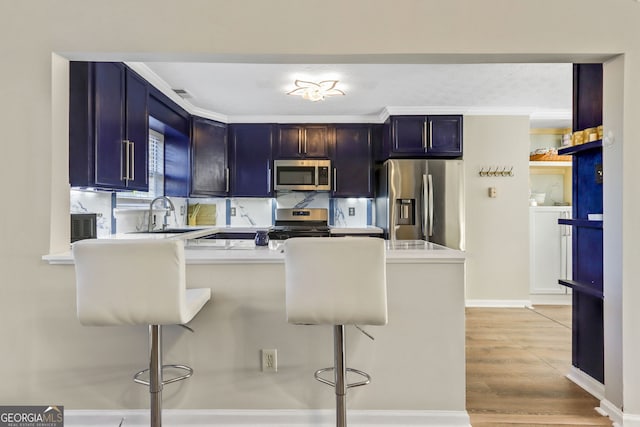 kitchen featuring light hardwood / wood-style flooring, ornamental molding, a kitchen bar, kitchen peninsula, and stainless steel appliances