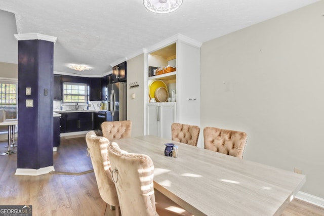 dining room featuring ornamental molding, sink, wood-type flooring, and a textured ceiling