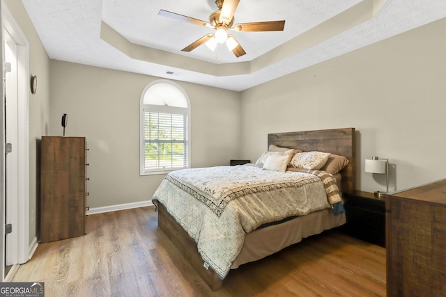 bedroom featuring hardwood / wood-style floors, a raised ceiling, and ceiling fan