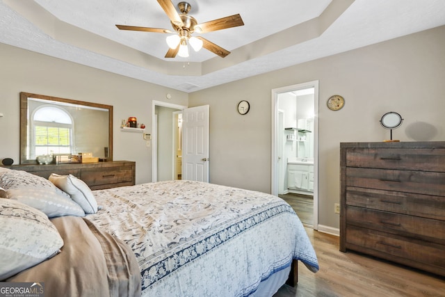 bedroom featuring wood-type flooring, connected bathroom, a raised ceiling, and ceiling fan