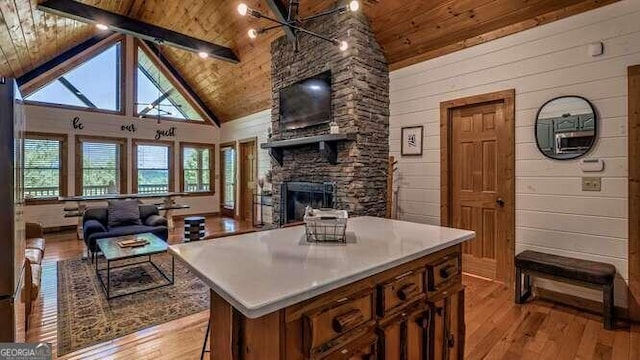 kitchen with wooden ceiling, high vaulted ceiling, a stone fireplace, a center island, and light wood-type flooring