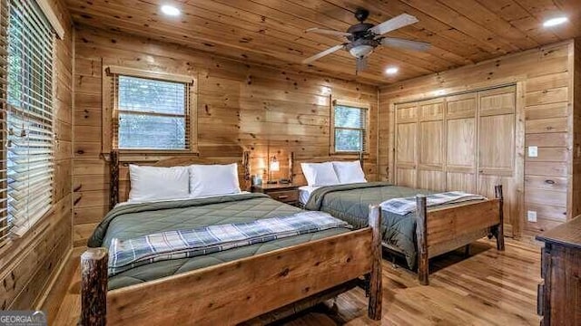 bedroom featuring light wood-type flooring, wooden walls, ceiling fan, and a closet