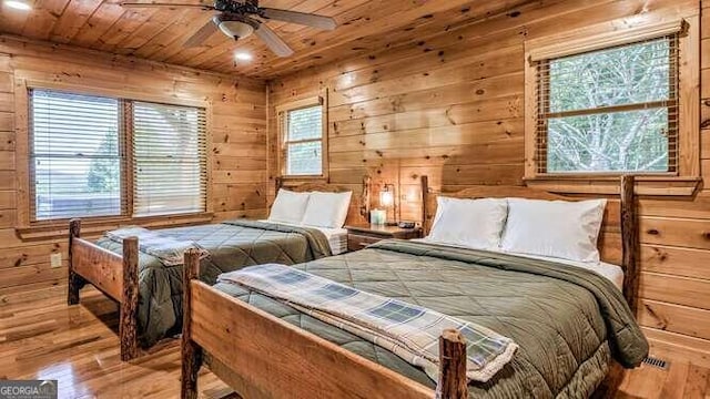 bedroom with light hardwood / wood-style floors, wooden walls, multiple windows, and ceiling fan