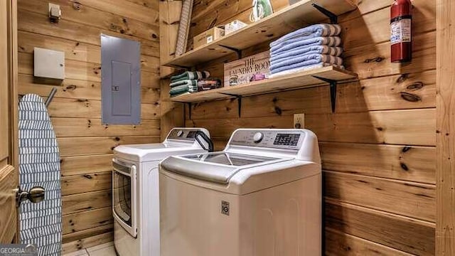 clothes washing area featuring electric panel, washer and dryer, and wooden walls