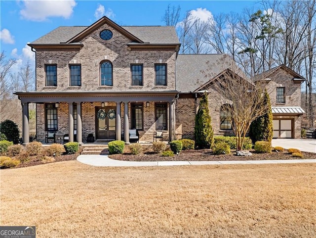 view of front facade with covered porch, french doors, a front yard, and brick siding