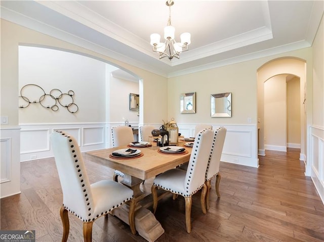 dining space featuring arched walkways, a tray ceiling, and wood finished floors