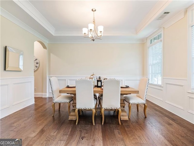 dining room with arched walkways, a raised ceiling, and a decorative wall