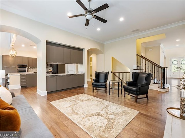 living room with arched walkways, ceiling fan, light wood-type flooring, and crown molding