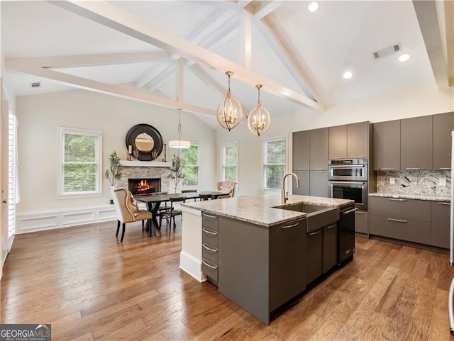 kitchen featuring gray cabinets, visible vents, a sink, an island with sink, and a lit fireplace