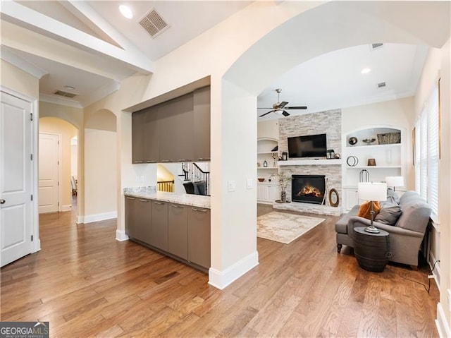 living area with visible vents, lofted ceiling, ceiling fan, light wood-style flooring, and built in shelves