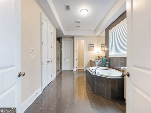 bathroom featuring tile patterned flooring, a garden tub, vanity, visible vents, and a tray ceiling