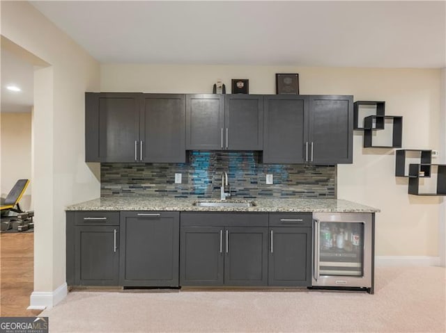 kitchen with wine cooler, a sink, decorative backsplash, and light stone countertops