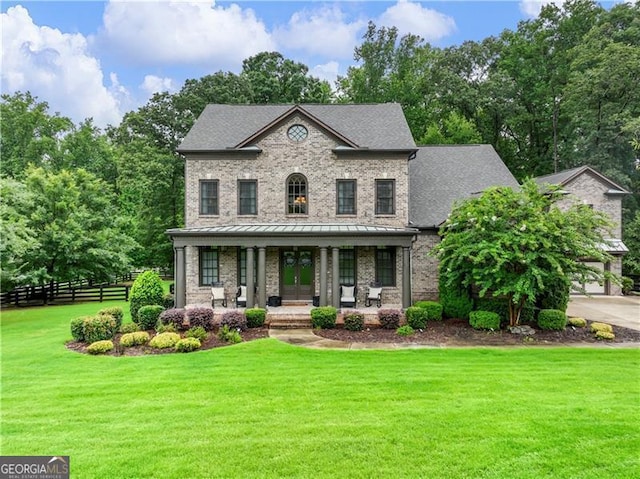 view of front of property with a shingled roof, covered porch, a standing seam roof, fence, and a front lawn