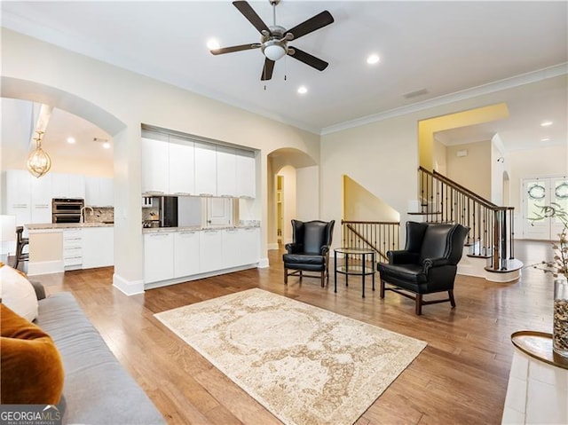 living area with arched walkways, ornamental molding, stairway, and light wood-style flooring