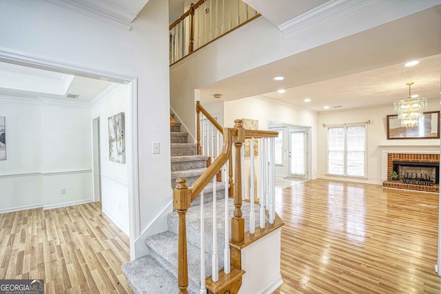 stairs featuring a brick fireplace, a notable chandelier, wood-type flooring, and ornamental molding