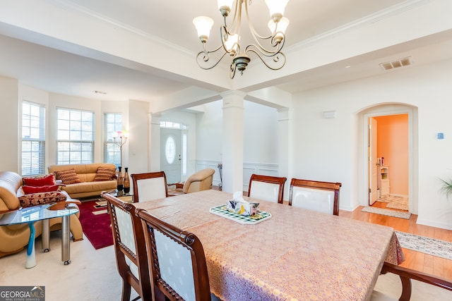 dining room featuring light wood-type flooring, a chandelier, ornamental molding, and decorative columns