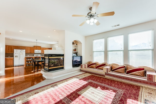 living room with built in features, a multi sided fireplace, tile patterned flooring, and ceiling fan