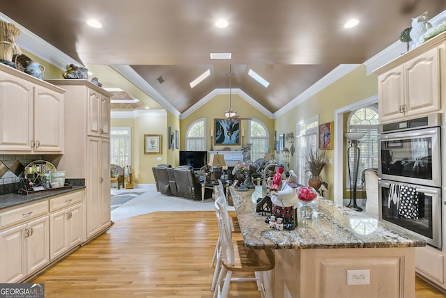 kitchen featuring dark stone counters, stainless steel double oven, vaulted ceiling with skylight, and a kitchen island