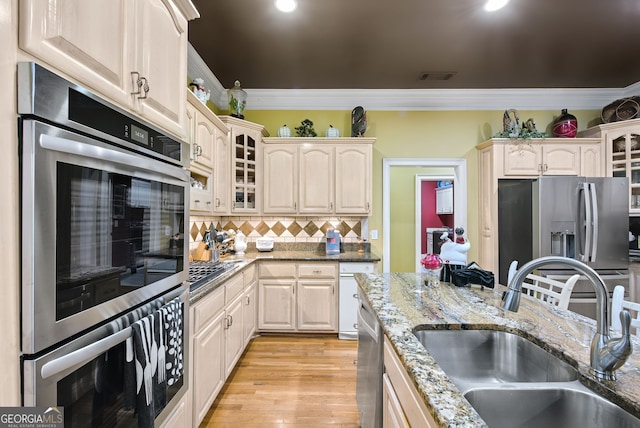 kitchen featuring stainless steel appliances, light stone counters, sink, crown molding, and light hardwood / wood-style flooring