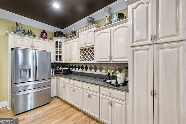 kitchen featuring tasteful backsplash, dark stone countertops, crown molding, stainless steel fridge, and light wood-type flooring