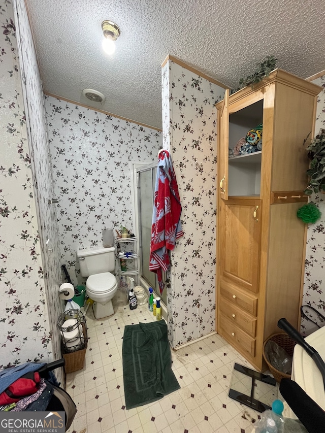 bathroom with toilet, a textured ceiling, crown molding, and a shower with shower door