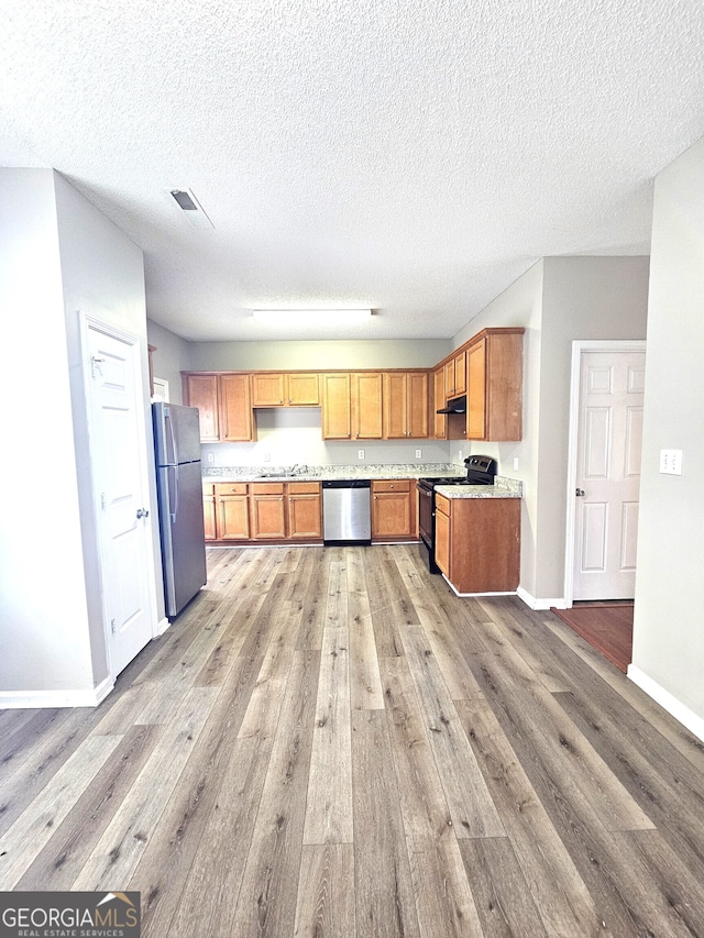 kitchen featuring stainless steel appliances, a textured ceiling, and light hardwood / wood-style flooring