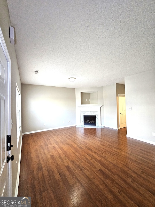 unfurnished living room featuring a premium fireplace, dark wood-type flooring, and a textured ceiling