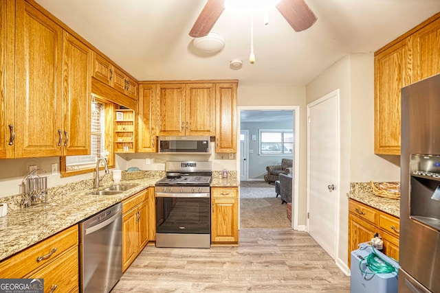 kitchen featuring light stone counters, stainless steel appliances, sink, light hardwood / wood-style floors, and ceiling fan