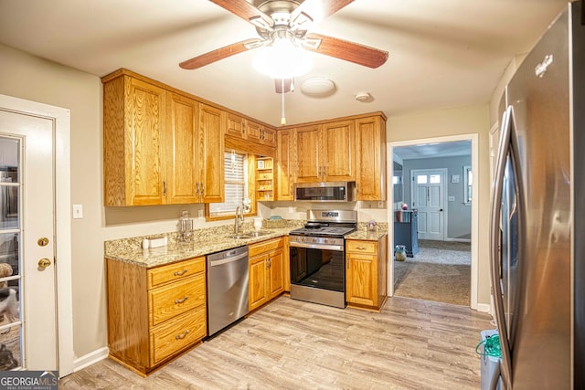 kitchen featuring light stone counters, stainless steel appliances, sink, ceiling fan, and light hardwood / wood-style flooring