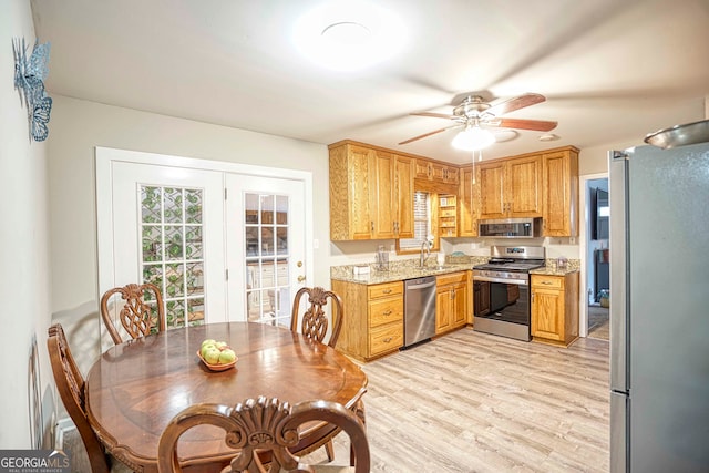 kitchen with light stone counters, sink, ceiling fan, light wood-type flooring, and appliances with stainless steel finishes