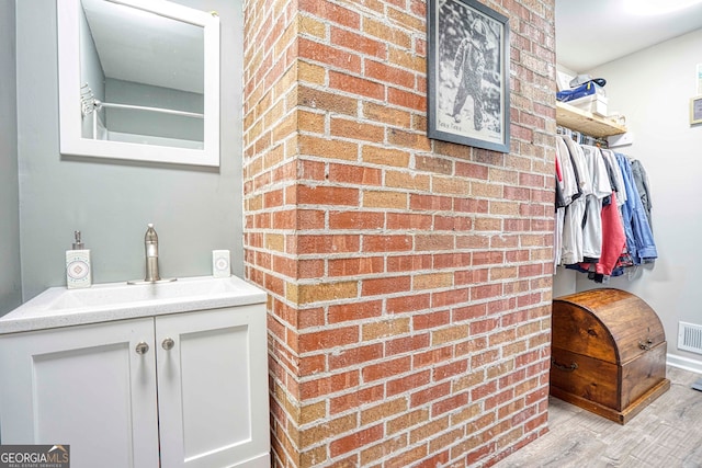 bathroom featuring vanity, hardwood / wood-style floors, and brick wall