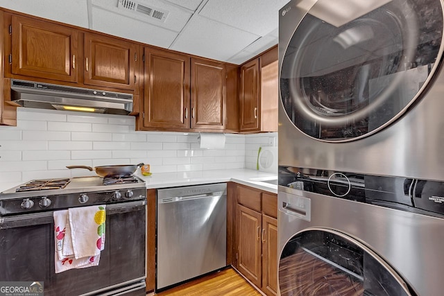 kitchen featuring wall oven, stainless steel dishwasher, a drop ceiling, gas stove, and stacked washer / drying machine