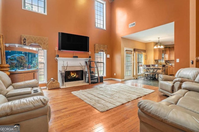 living room with a towering ceiling, light hardwood / wood-style floors, and a chandelier