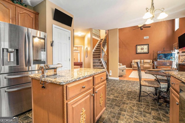 kitchen featuring ceiling fan with notable chandelier, light stone counters, a center island, decorative light fixtures, and stainless steel fridge