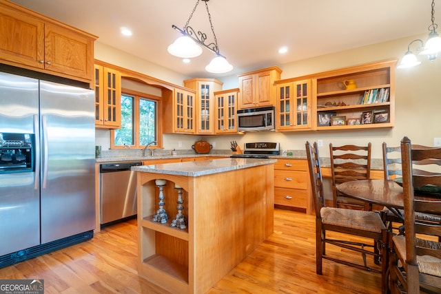 kitchen with a center island, light stone countertops, decorative light fixtures, light hardwood / wood-style floors, and stainless steel appliances