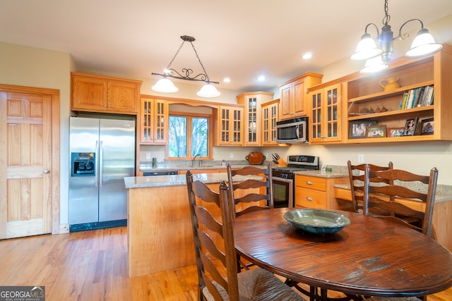 kitchen featuring light hardwood / wood-style floors, light stone countertops, hanging light fixtures, and appliances with stainless steel finishes