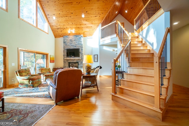 living room with a stone fireplace, light hardwood / wood-style flooring, high vaulted ceiling, and wood ceiling